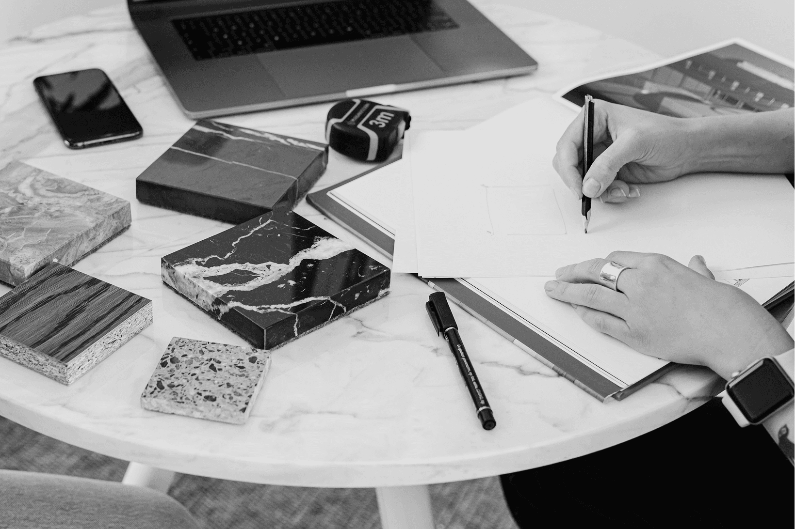 Interior designer reviewing fitout drawings with material samples including marble, timber, and terrazzo swatches on a marble table — Nodus Group design process