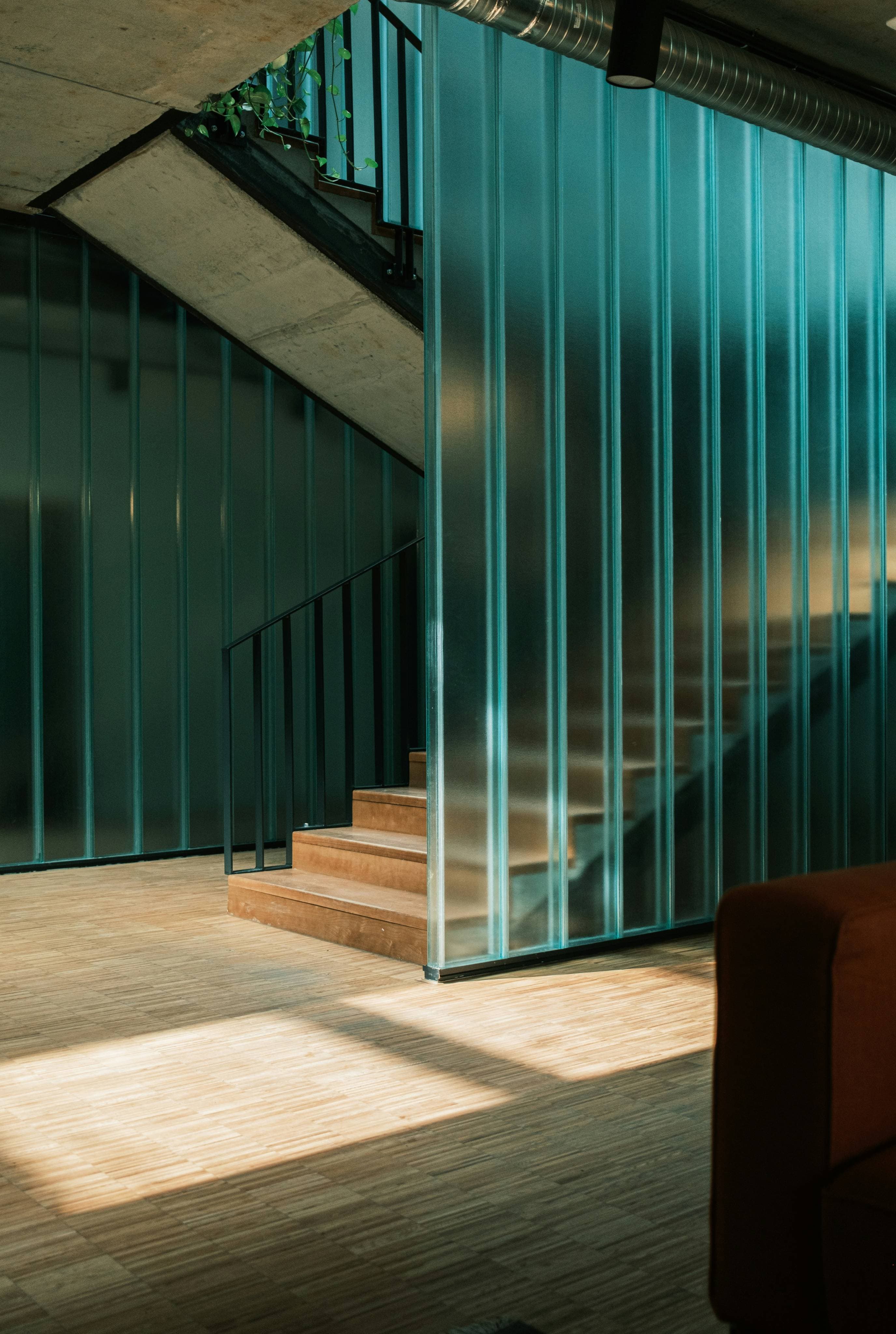 Commercial fitout staircase with ribbed teal glass partition, exposed concrete soffit, timber stair treads, and industrial ducting